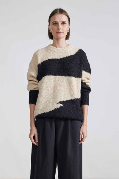 Front view of model wearing black and cream sweater with pushed up sleeves