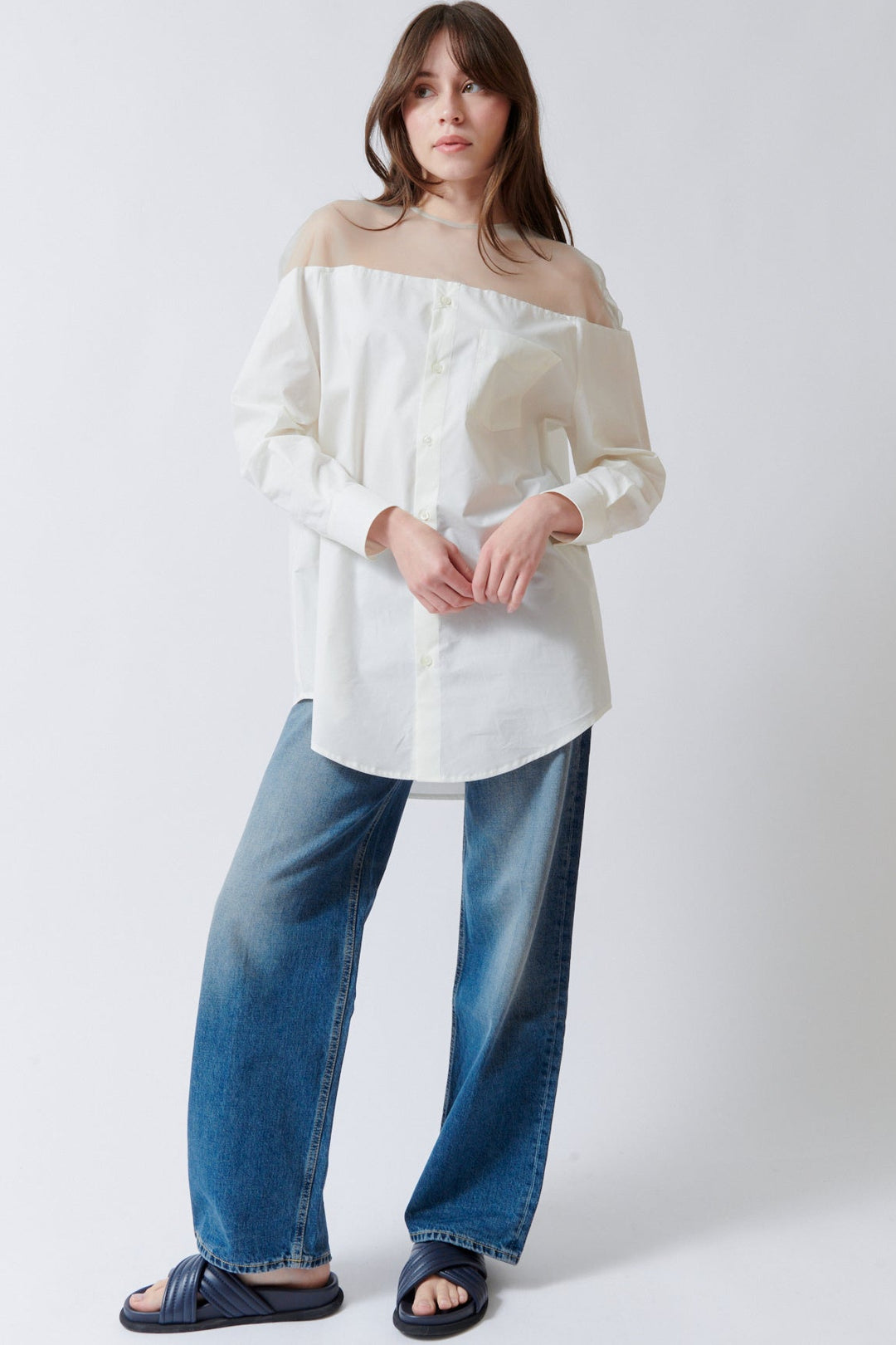 Woman wearing a white off-shoulder top and blue jeans against a white background
