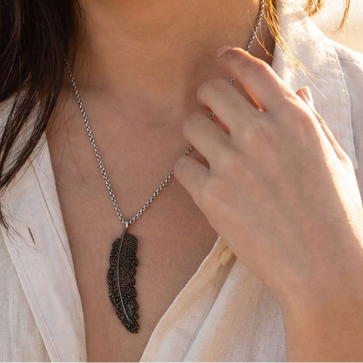 Person wearing a feather pendant necklace with a soft focus background