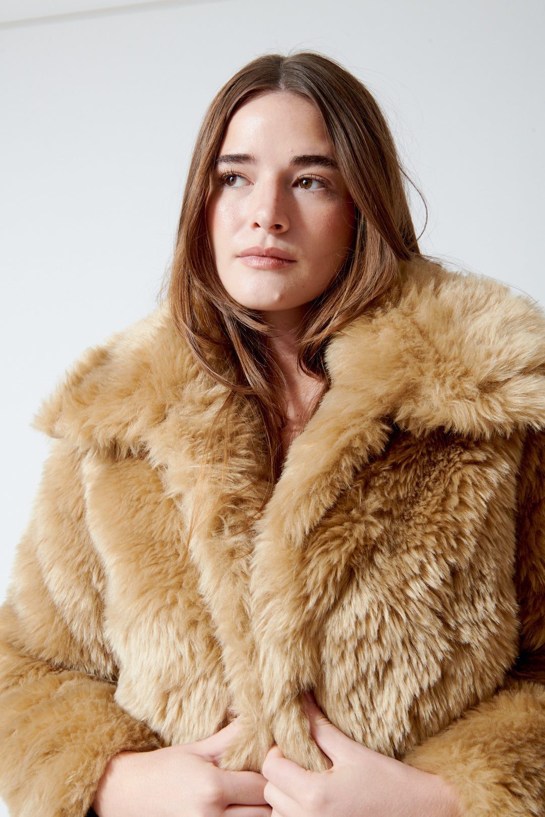 A woman wearing a meimeij plush, shaggy faux fur coat in a warm camel tan color, posed against a plain light gray background.