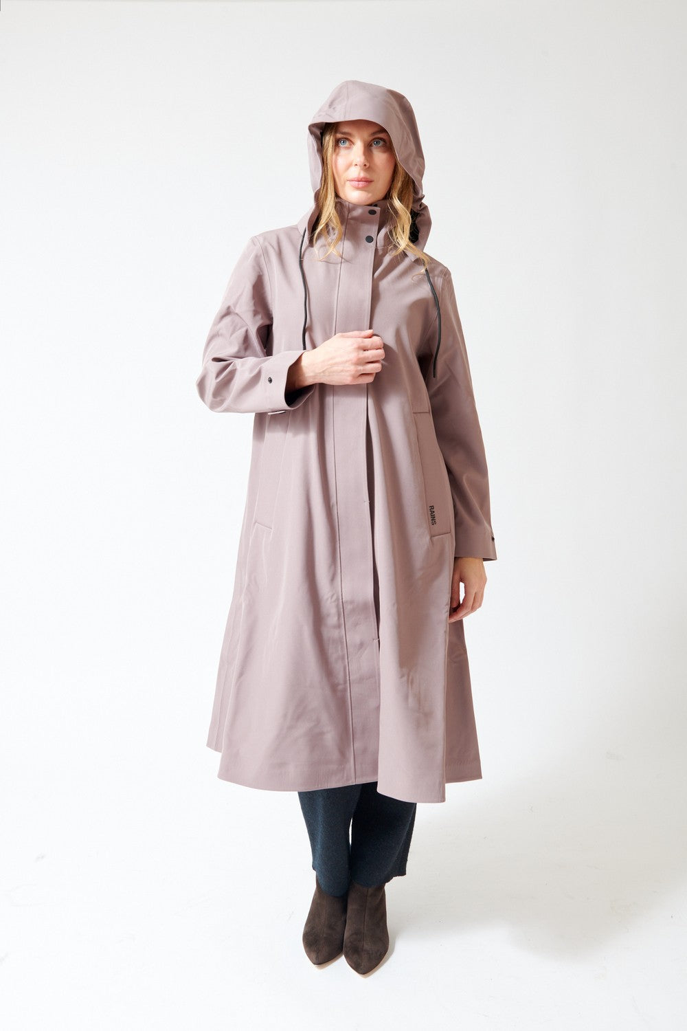 A woman modeling a long, hooded raincoat in a muted dusty mauve color, standing against a plain white studio background.