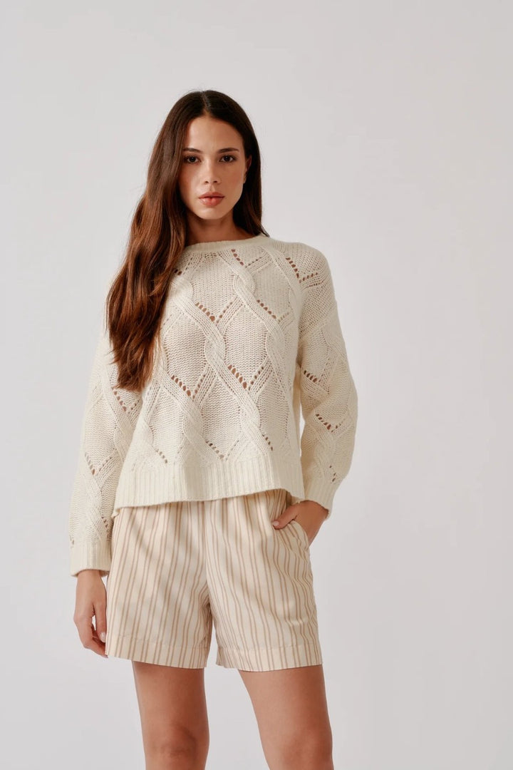 Woman wearing a cream-colored knit sweater and shorts on a plain background
