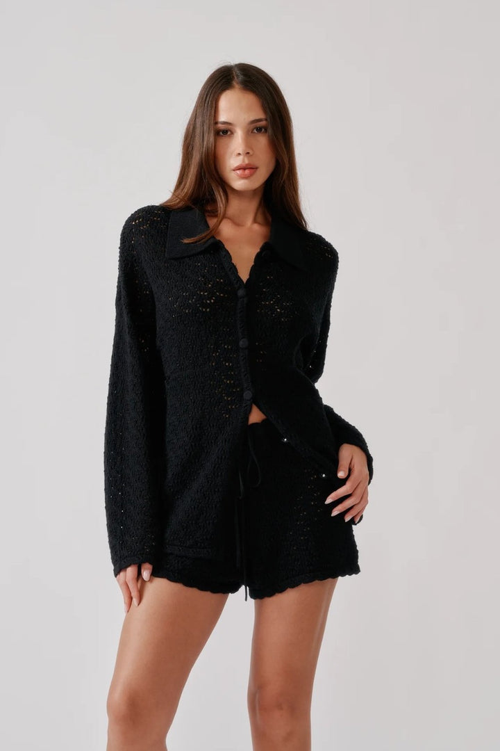 Model wearing the Sablyn Crochet relaxed button up shirt  called Izzy in black sold at Grethen House, with shorts in front of a white background