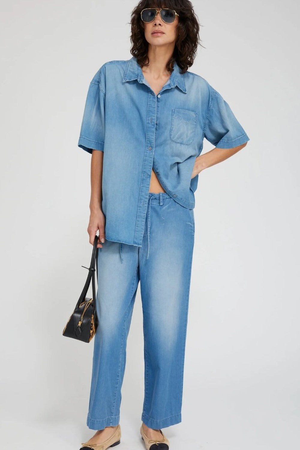Person wearing a blue denim outfit with sunglasses on a white background