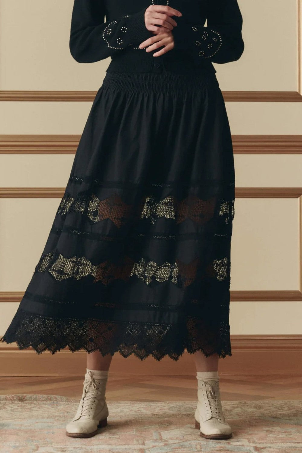 Person wearing The Great  Rosette black crochet skirt with floral embroidery, sold at Grethen House, standing against a beige wall.