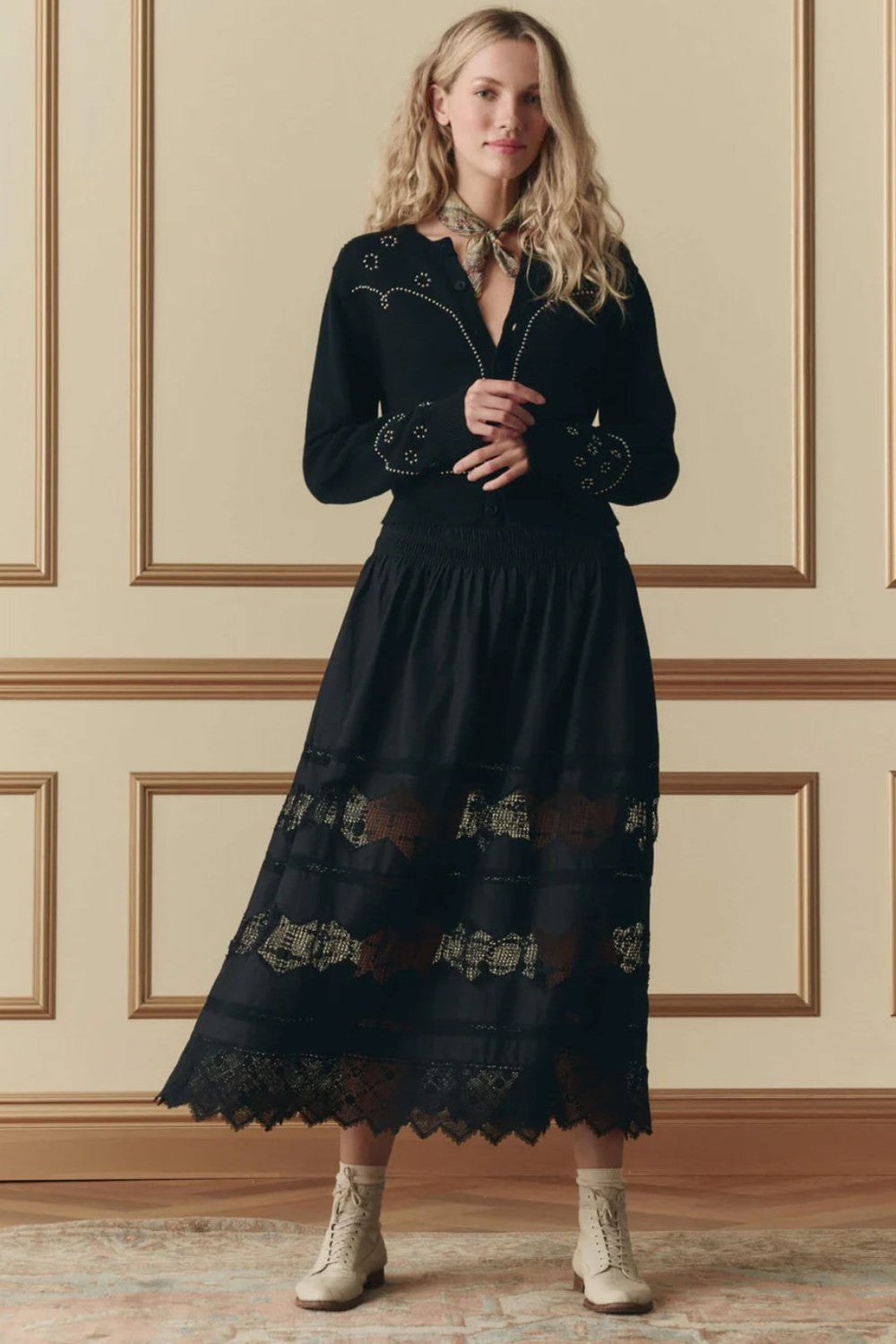A woman wearing The Great  Rosette black crochet skirt with floral embroidery sold at Grethen House. Model standing against a beige wall.