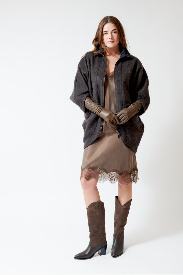 A woman modeling a dark charcoal gray coat over a brown dress with a lace hem, paired with brown leather gloves and brown knee-high boots, against a plain white studio background.